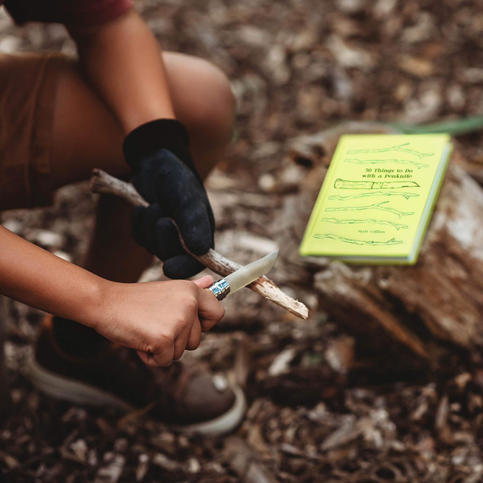 Boy doing wood whittling in forest using 50 Things to do with a Penknife book by Matt Collins with advanced No08 wood whittling knife by Opinel, sold by Your Wild Books in a bundle for 13% off