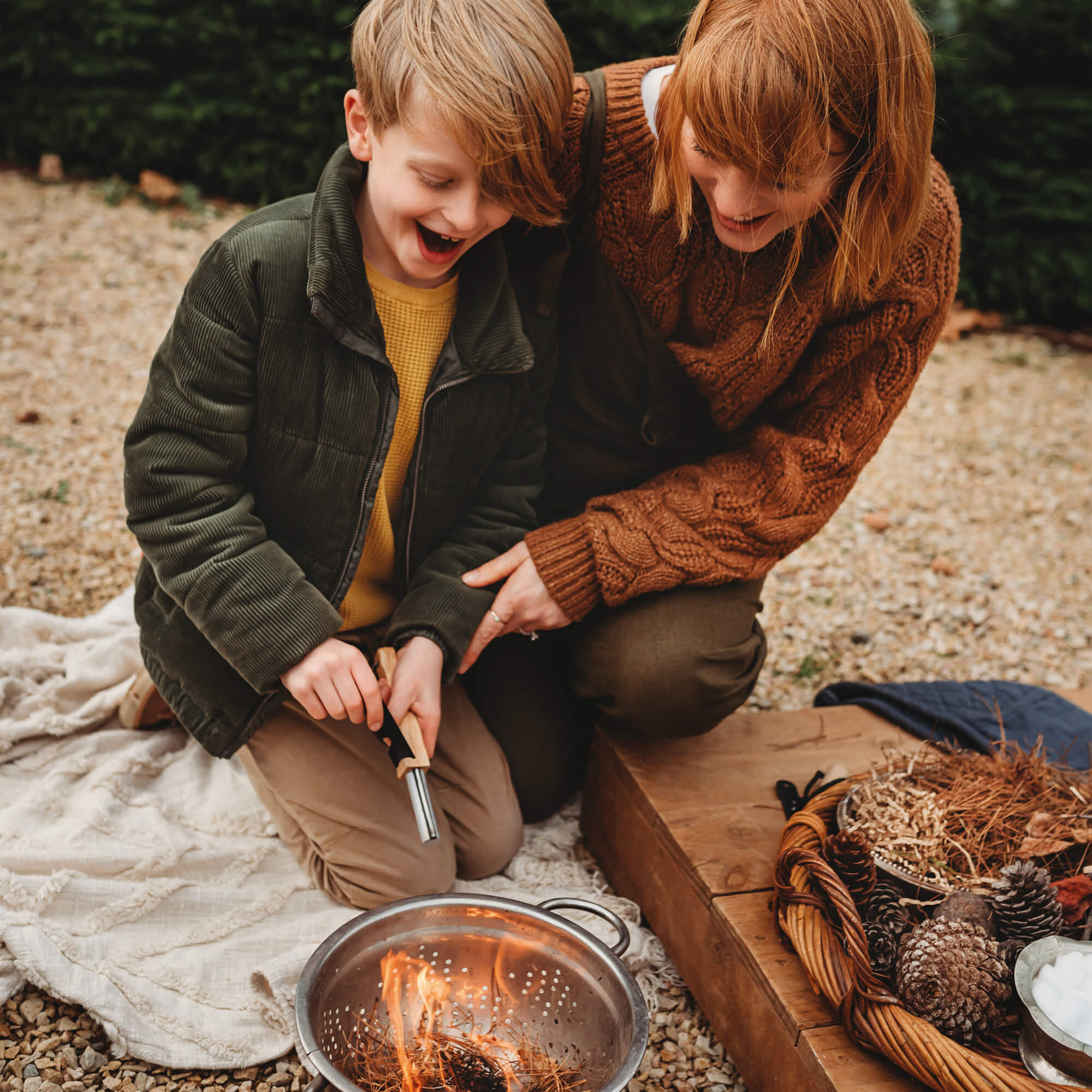 Joyous face of boy starting a fire using flint and stone style fire starter with wooden handle with kindling made by Your Wild Books