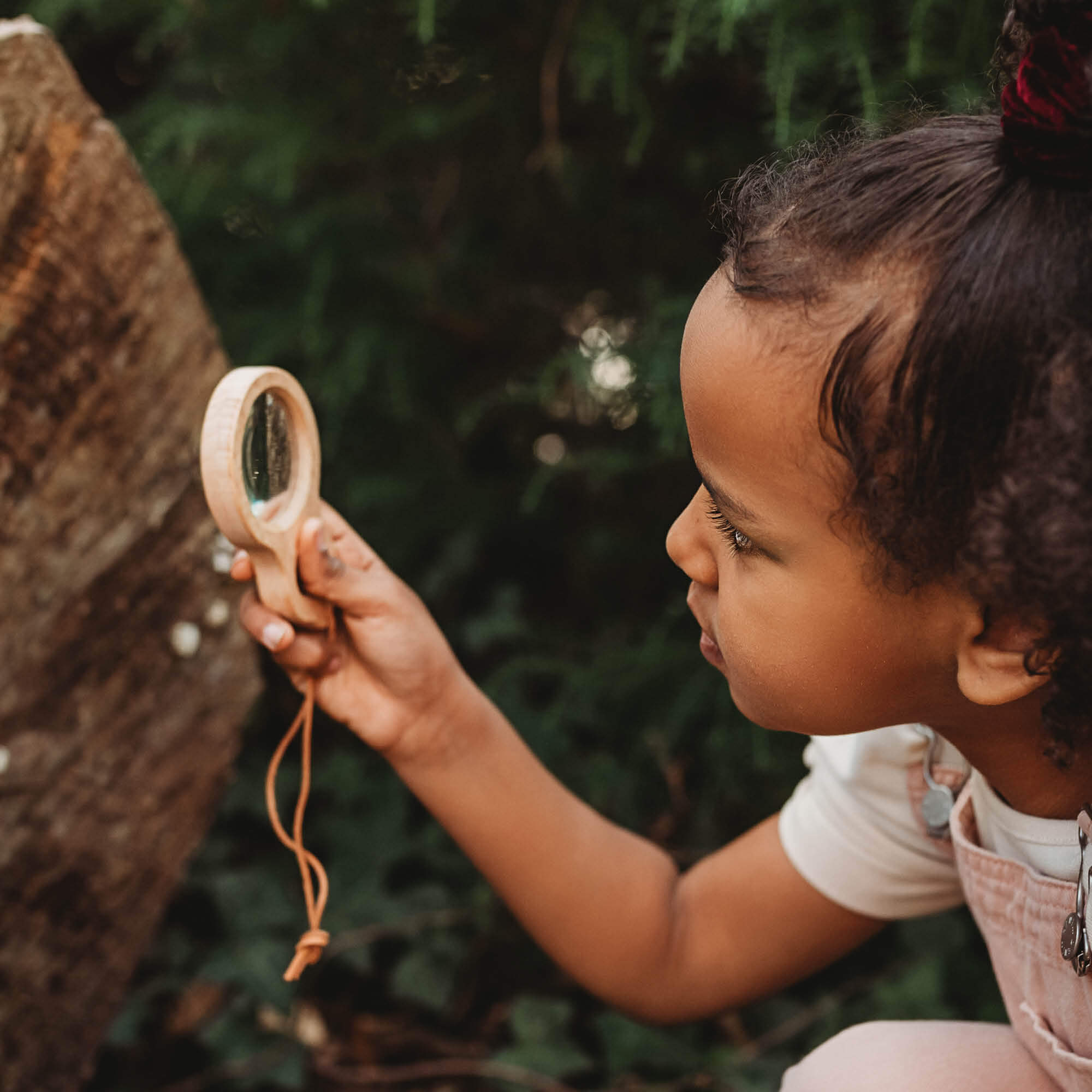 Girl holding Kikkerland dual magnifier wooden magnifying glass with two lenses for exploring nature and play from Your Wild Books
