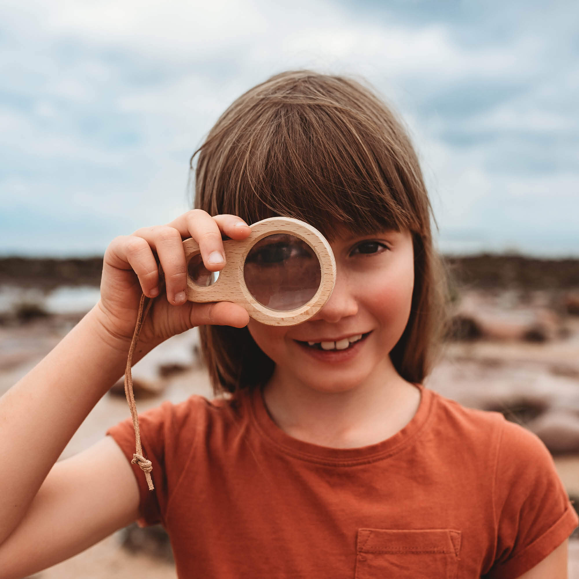 Girl holding Kikkerland dual magnifier wooden magnifying glass with two lenses for exploring nature and play from Your Wild Books
