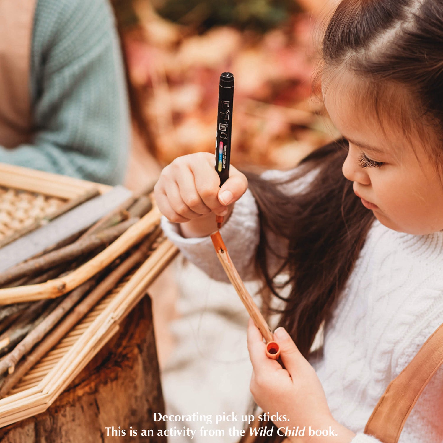 Child colouring the end of a whittled stick to make DIY pick up sticks game,  a nature craft activity from Your Wild Books that have been decorated with paint pens from Life of Colour