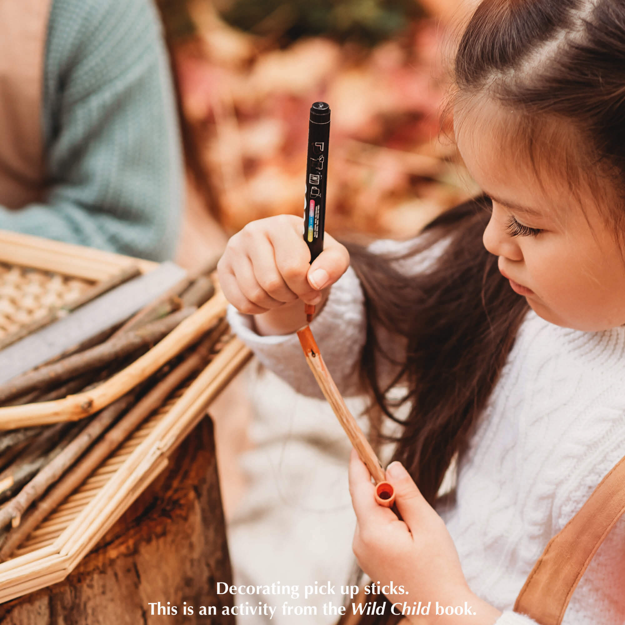 Child colouring the end of a whittled stick to make DIY pick up sticks game, a nature craft activity from Your Wild Books that have been decorated with paint pens from Life of Colour