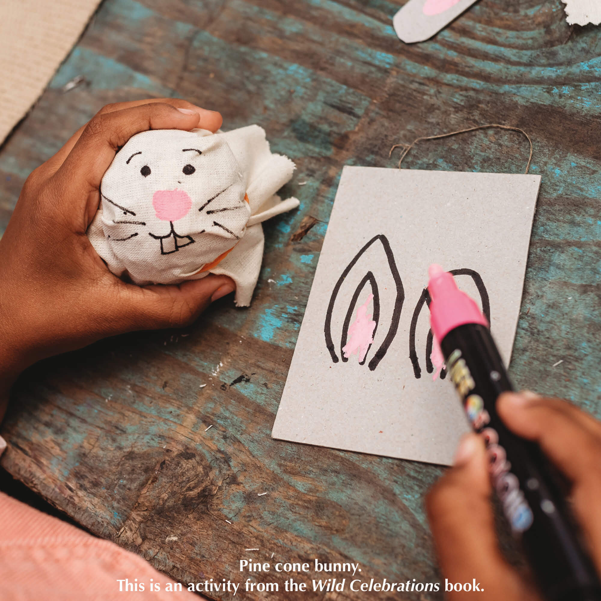 Child making pine cone bunny drawing on fabric and cardboard from nature craft activity from Your Wild Books that have been decorated with paint pens from Life of Colour