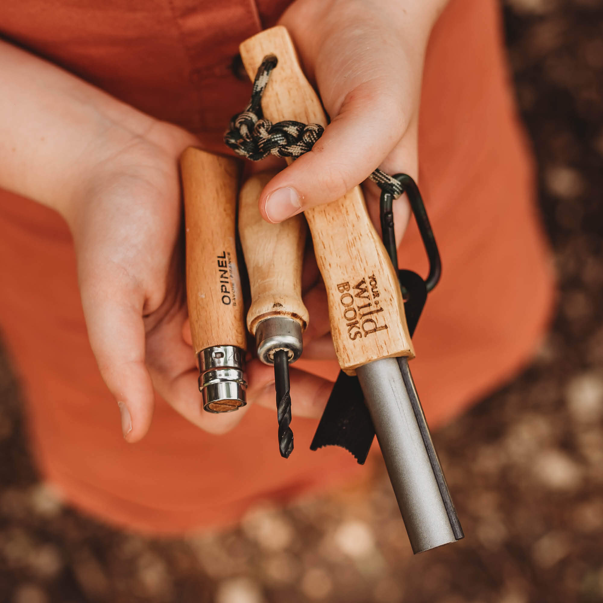 Child holding the three tools from Real Tools Bundle by Your Wild Books includes Wild Projects for Families book, whittling knife, hand drill and fire starter.