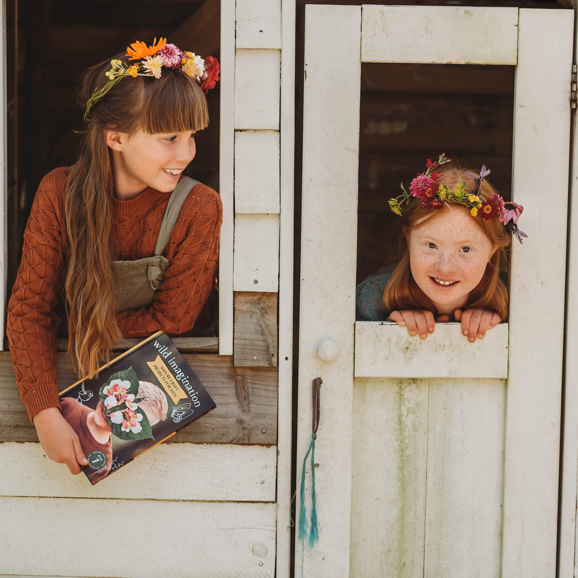 Two girls in a cubby house wearing flower crowns they made from Wild Imagination, nature craft projects for kids book, made in Australia by Your Wild Books.