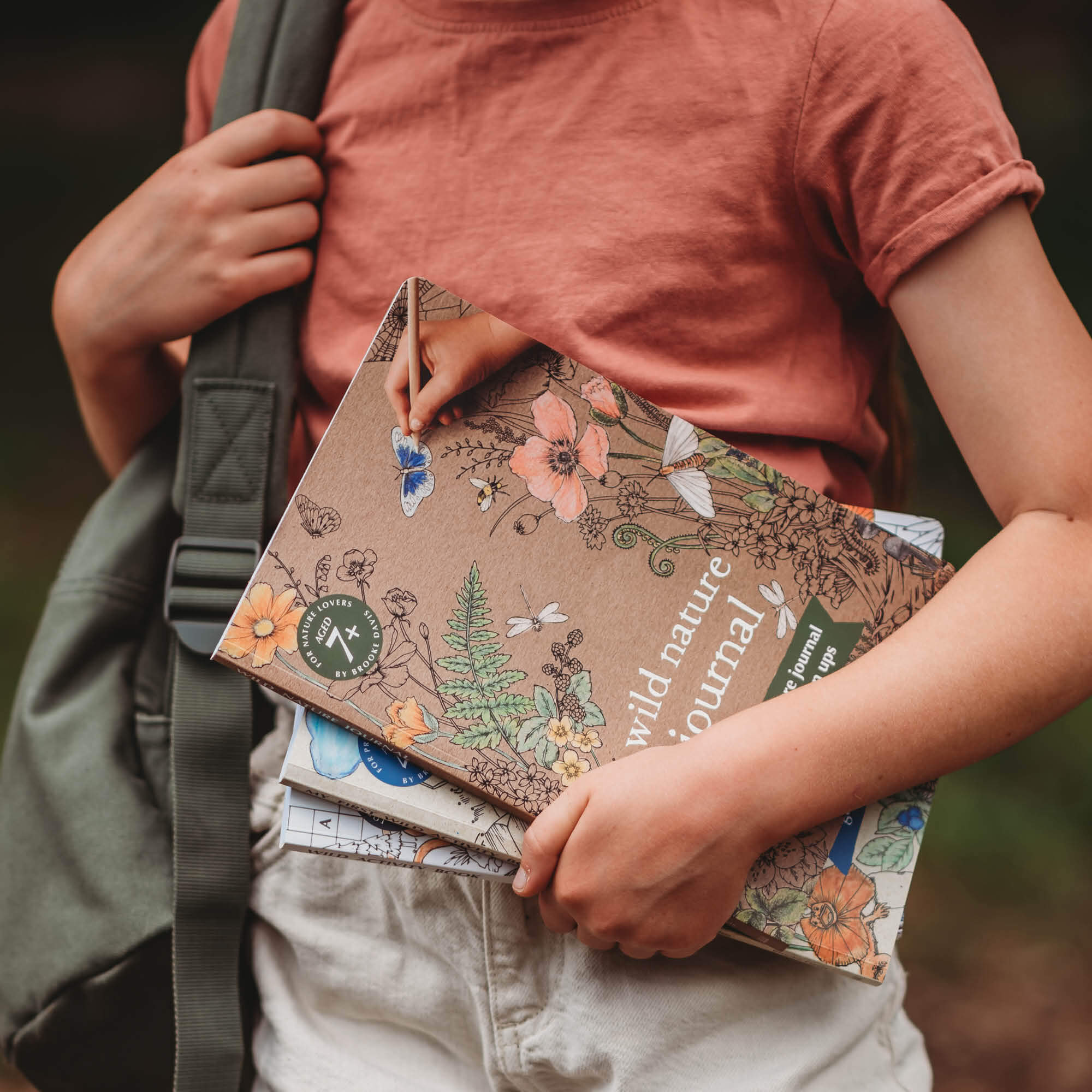 Child holding stack of books including Wild Nature Journal, a guided nature journal for kids and grown ups is made in Australia by Your Wild Books.