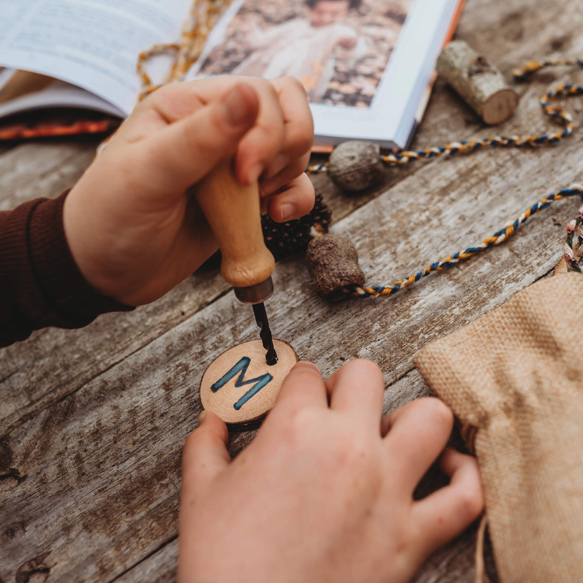 Drilling into a small piece of wood with a kid size hand drill with wooden handle and hessian style bag great for nature craft and woodworking projects from Your Wild Books