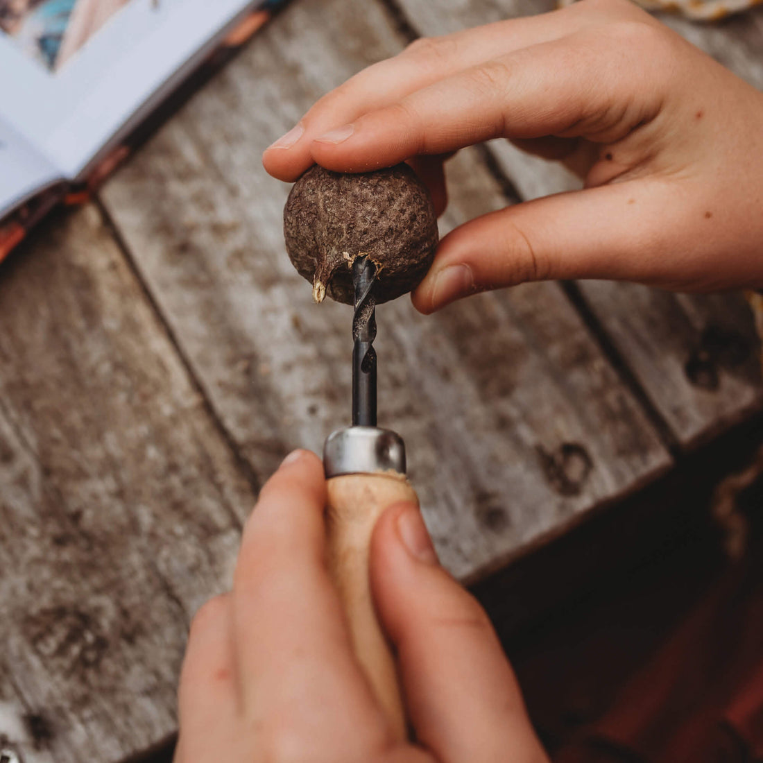 Drilling into a gum nut with a kid size hand drill with wooden handle and hessian style bag great for nature craft and woodworking projects from Your Wild Books