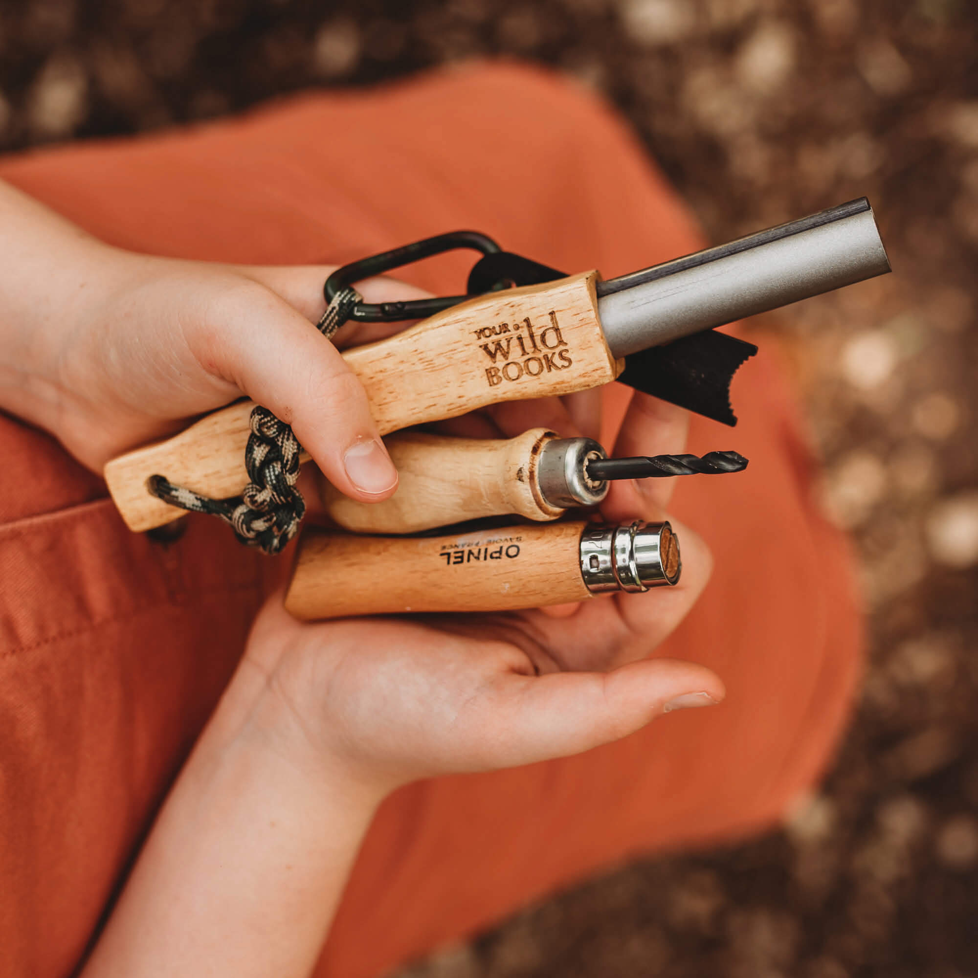 Childs hands showing tools including Drilling into a gum nut with a kid size hand drill with wooden handle whittling knife and fire starter great for nature craft and woodworking projects from Your Wild Books