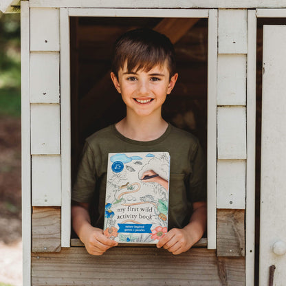 Child smiling and holding My First Wild Activity Book for kids 4-7 years who are learning to read, featuring nature inspired games and puzzles.
