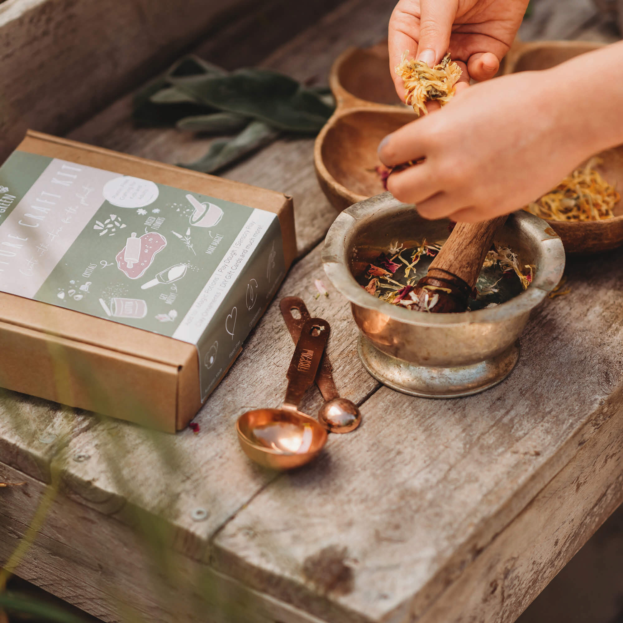 Child making magic potion using Nature craft kit by Little Wild and Green made with all natural materials including 4 bags of petals, 2 paint powders, 1 eco glitter, a box of crystal chips and a wooden spoon. perfect for nature crafting for kids including playdough, clay and magic potions from Your Wild Books