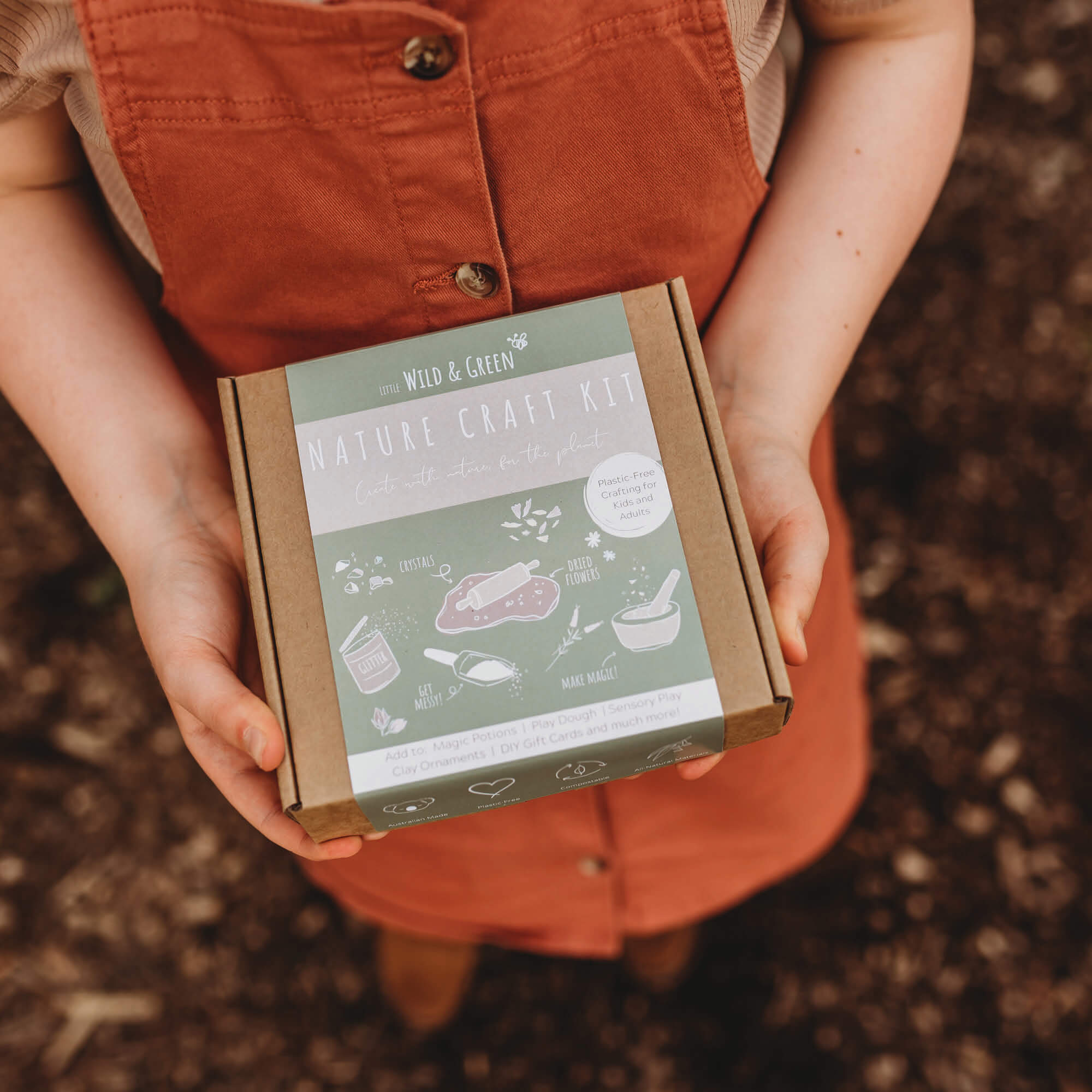 Child holding Nature craft kit by Little Wild and Green made with all natural materials including 4 bags of petals, 2 paint powders, 1 eco glitter, a box of crystal chips and a wooden spoon. perfect for nature crafting for kids including playdough, clay and magic potions from Your Wild Books