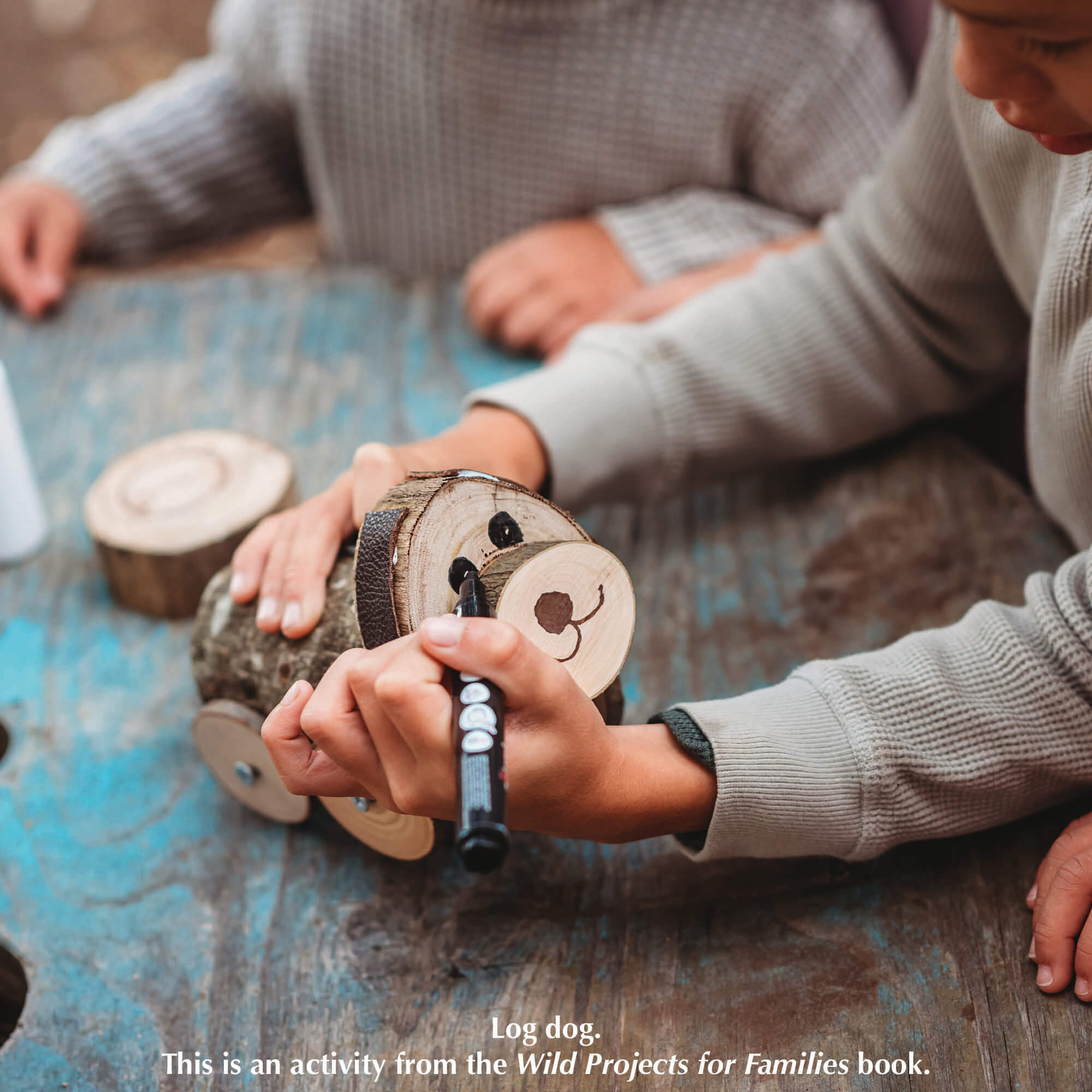 A child drawing a face on a log dog,  a nature craft activity from Your Wild Books that have been decorated with paint pens from Life of Colour