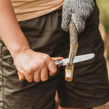 Child peeling bark from a stick wearing a whittling glove. Wood whittling knives for kids for all your nature craft projects, suitable for beginners and advanced woodworkers. Made by Opinel from Your Wild Books.