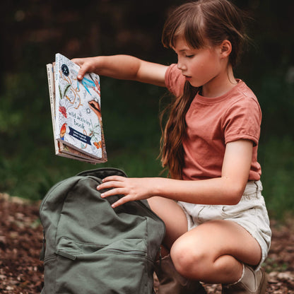 Child putting books into bag, Wild Activity Book, nature inspired games and puzzles by Your Wild Books. Made in Australia for kids over 7 years.