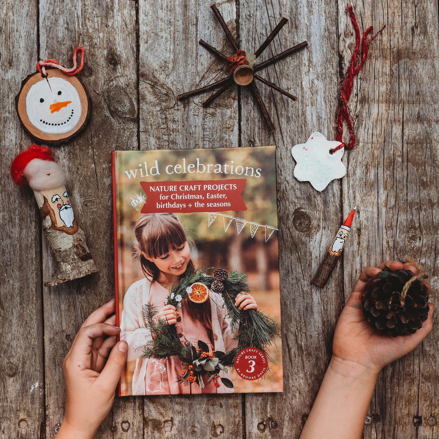 Child holding DIY Christmas decorations made with nature and the book Wild Celebrations from the Nature Craft Series by Your Wild Books is printed in Australia using FSC Certified paper.