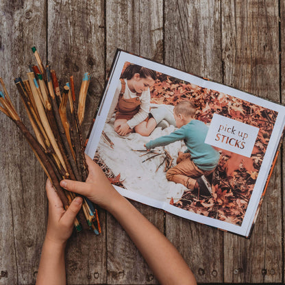 Child holding DIY pick up sticks game they whittled from wood and coloured with paint pens. Step by step instructions found in Wild Child, nature craft projects for kids book, made in Australia by Your Wild Books. 