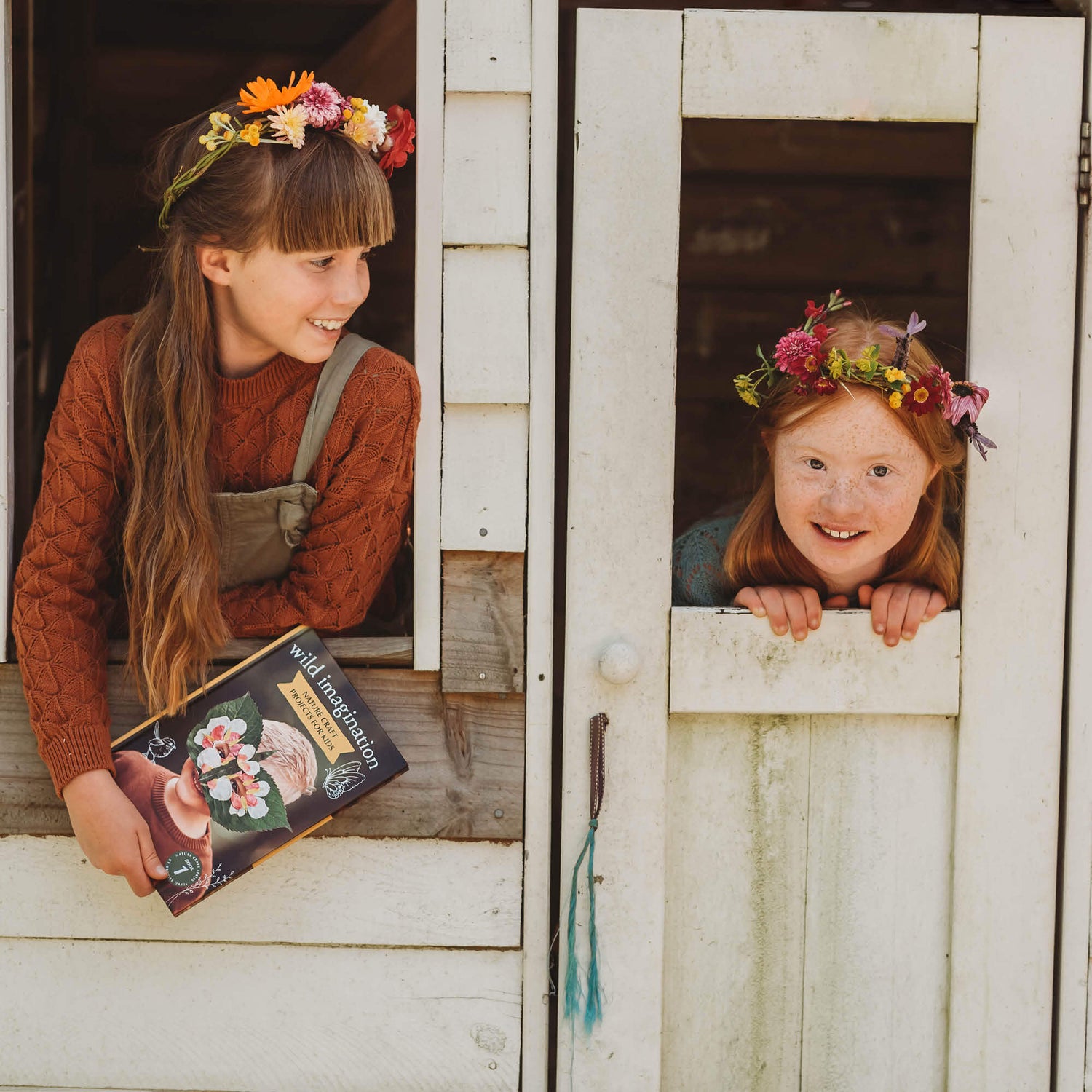Two girls in a cubby house wearing flower crowns they made from Wild Imagination, nature craft projects for kids book, made in Australia by Your Wild Books. 