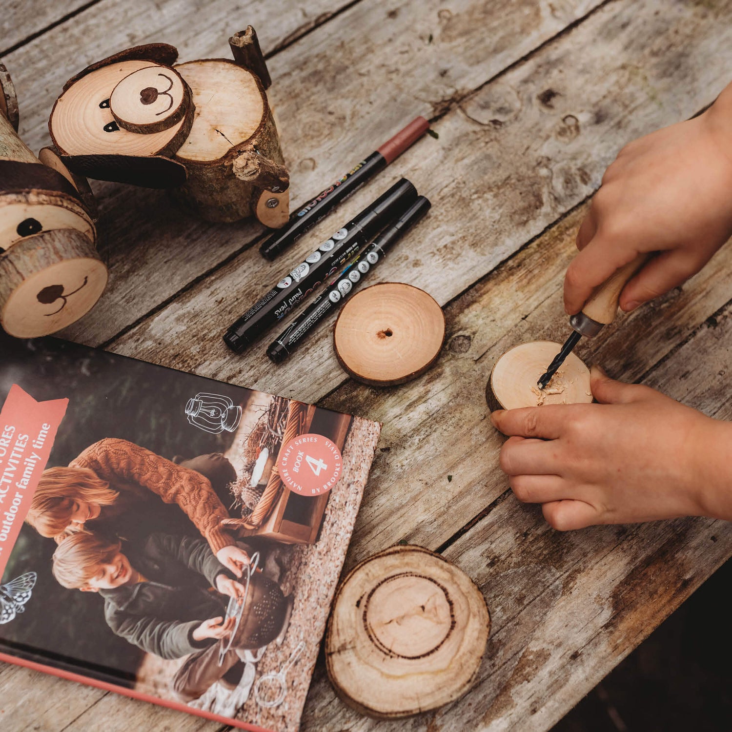 Child drilling a hole in wood to make a log dog from Real Tools Bundle by Your Wild Books includes Wild Projects for Families book, whittling knife, hand drill and fire starter.